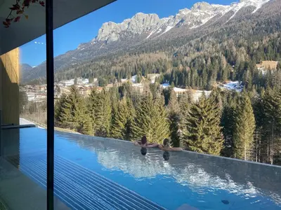 two people swimming in a pool with mountains in the background at Latemar - Hotel Suites Spa in Soraga