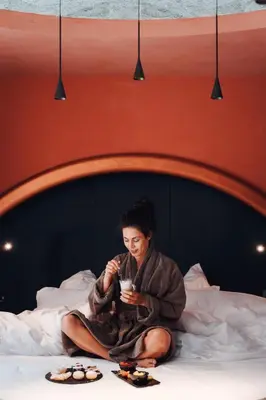 a woman in a robe sitting on a bed at Latemar - Hotel Suites Spa in Soraga
