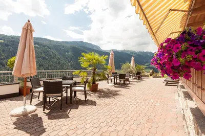 a patio with chairs tables and umbrellas and flowers at Residence Garni Melcherhof in Racines