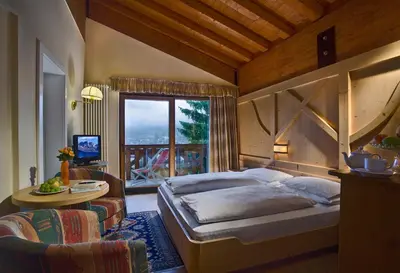 a bedroom with a bed and a table and a window at Hotel Catinaccio Rosengarten in Moena