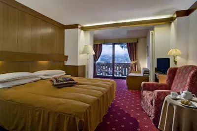 a hotel room with a bed and a chair and a window at Hotel Catinaccio Rosengarten in Moena