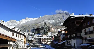 a town with snow covered buildings and a mountain at Hotel Catinaccio Rosengarten in Moena