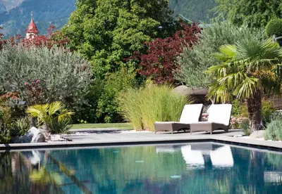 a swimming pool with two chairs next to a garden at Hotel Ortler in Tirolo