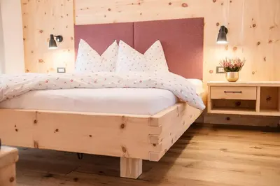 a bedroom with a wooden bed with white sheets at Alpine Chalets App. Pichlerhof in Brunico