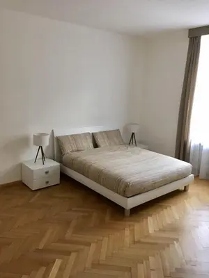 a white bedroom with a bed and a wooden floor at Appartamento Nadia in Merano