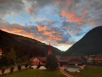 a sunset over a village with a church in the mountains at MANTANA - Apartments in San Lorenzo di Sebato