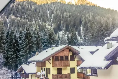 a house covered in snow with a mountain in the background at Residence Des Alpes in Canazei