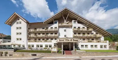 a large white building with a sign in front of it at Aparthotel Wellness Villa di Bosco in Tesero