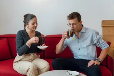 a man and a woman sitting on a couch drinking coffee at Hotel Erica in Tesero