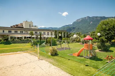 a playground in front of a building with mountains in the background at Hotel Mandelhof in Appiano sulla Strada del Vino