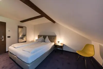 a bedroom with a large bed and a yellow chair at Hotel Mandelhof in Appiano sulla Strada del Vino