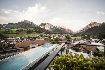 a person holding a glass of beer in front of a fireplace at Excelsior Dolomites Life Resort in San Vigilio Di Marebbe