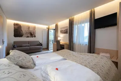 a bedroom with two white beds and a couch at Hotel Canada in Predazzo