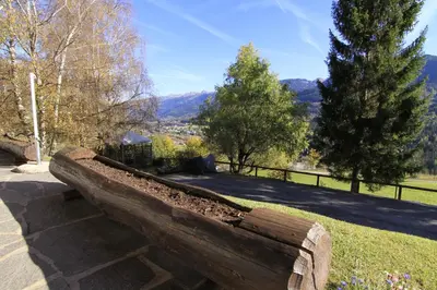 a wooden bench in a park with mountains in the background at Hotel Panorama in Cavalese