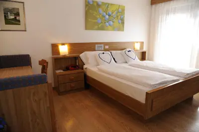 a bedroom with a bed and a chair and a window at Hotel Sole Family Hotel in Predazzo