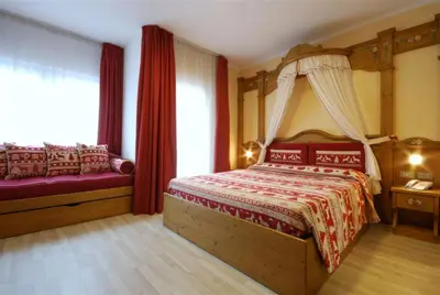 a bedroom with a canopy bed and red curtains at Hotel Bellaria in Predazzo