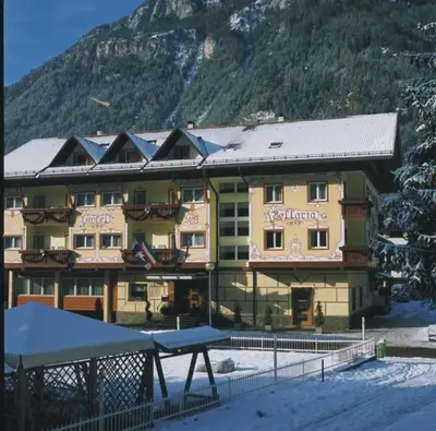 a large building in the snow in front of a mountain at Hotel Bellaria in Predazzo
