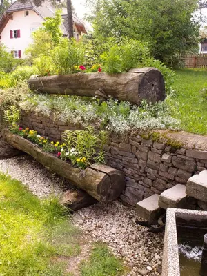 a garden with two logs and flowers on a stone wall at Schönblick OHG des Daum Tobias in Aldino