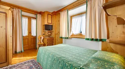 a bedroom with a bed and a desk and windows at Hotel Natale in Cortina dʼAmpezzo