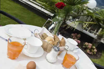 a table with a basket of bread and a vase with a rose at Hotel Finkenhof - Feel at home in Schenna