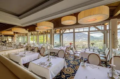 a restaurant with white tables and chairs and windows at Hotel Finkennest - Panoramic Garden Resort in Schenna