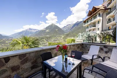 a balcony with a table and chairs and mountains at Hotel Finkennest - Panoramic Garden Resort in Schenna