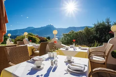 a restaurant with tables and chairs with mountains in the background at Landhaus Hotel Kristall in Marlengo