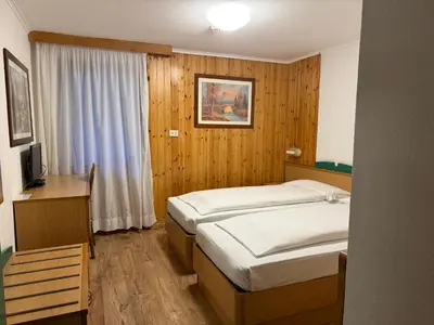 a bedroom with two beds and a desk with a television at Sport Hotel Pampeago in Tesero