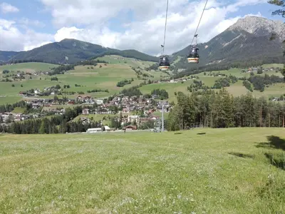 a gondola ride over a green field with a town at Alfred Ties Apartments in San Vigilio Di Marebbe