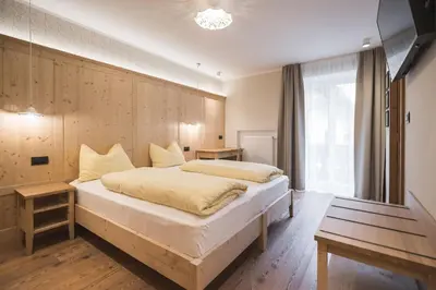 a bedroom with a large bed with a wooden wall at Emma Historic Hotel in Villabassa