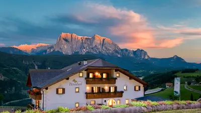 a house with a balcony with mountains in the background at Hotel-Chalet Pennhof in Barbiano