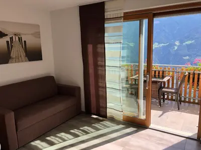 a room with a couch and a balcony with a table at Rofenhof in Naturno