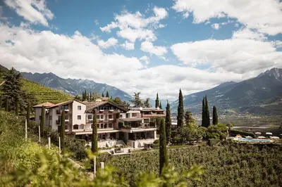a building on a hill with trees and mountains at Das Grafenstein Familienresidence in Cermes