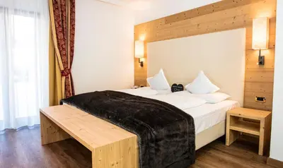 a bedroom with a large white bed with a black blanket at Hotel Dorfer Alpine&Charming in Selva di Val Gardena