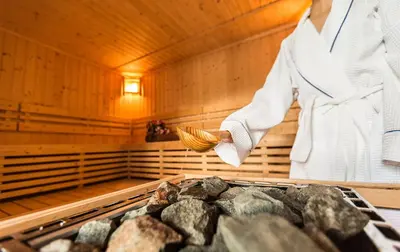 a woman standing in a sauna holding a brush at Das Bergland - Vital & Activity in San Leonardo in Passiria