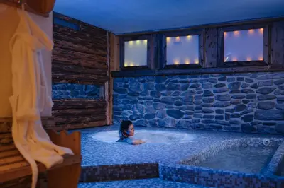 a woman in a bath tub in a room with a stone wall at Hotel La Montanara Predazzo in Predazzo