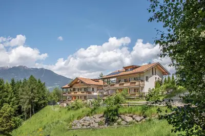a large house on a hill with mountains in the background at Apartmenthaus Fuchsmaurer in Bressanone