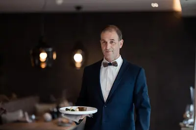 a man in a suit holding a plate of food at Chalet PURMONTES in San Lorenzo di Sebato