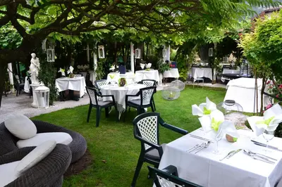 a table with white tables and chairs under a tree at Hotel Villa Groff in Ora/Auer