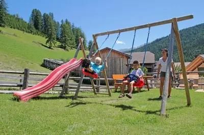 a woman and two children playing on a swing at Dolomites Apartments Ciasa Vally in San Cassiano