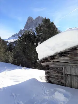 a log cabin covered in snow with a mountain in the background at Lehrnerhof Lüsen in Luson