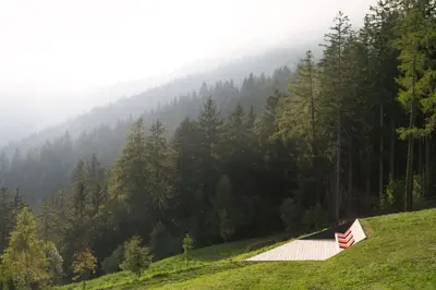 a barn on the side of a hill with a forest at Vigilius Mountain Resort in Lana