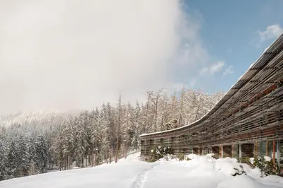 a building covered in snow next to a forest at Vigilius Mountain Resort in Lana