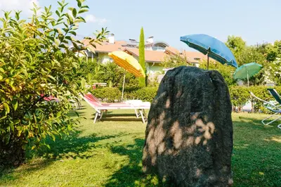 a rock in a yard with a table and umbrellas at Bio Hotel Kaufmann in Ora/Auer