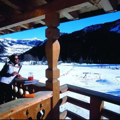 a man sitting on a wooden porch with a ski slope at Residence Vila in Colfosco