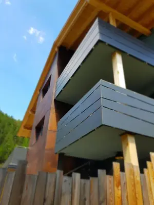 a building with a blue balcony on top of a wooden fence at Klimahouse North in Campitello di Fassa