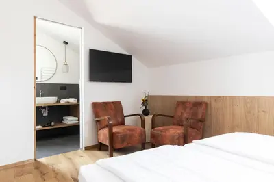 a bedroom with two chairs and a bed and a mirror at Garni Hotel Tauber in Bressanone