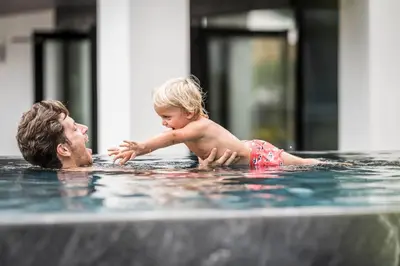 a man and a child playing in a swimming pool at Biancaneve Family Hotel in Selva di Val Gardena