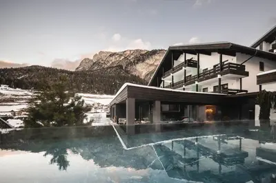 a hotel with a swimming pool in front of a mountain at Biancaneve Family Hotel in Selva di Val Gardena