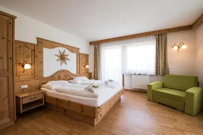 a bedroom with a large bed and a green chair at Garni Hotel Bel Vert in Selva di Val Gardena